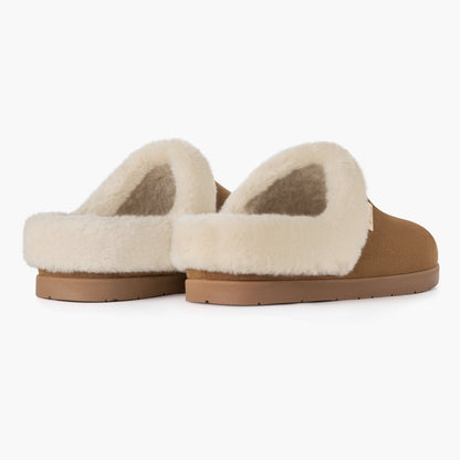 A pair of PCSsole slip-on mule slippers with a tan faux-leather upper, cream-colored shearling-style lining, and a tan sole