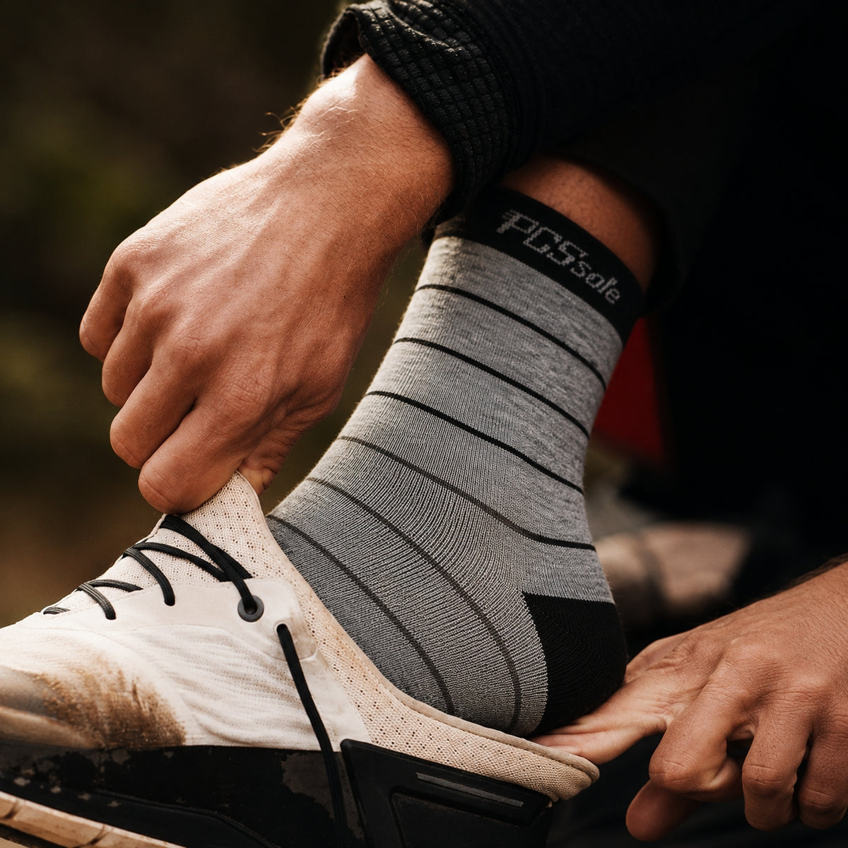 A person putting on a gray-and-black striped athletic crew sock with 'PCSsole' branding, paired with a white athletic shoe.