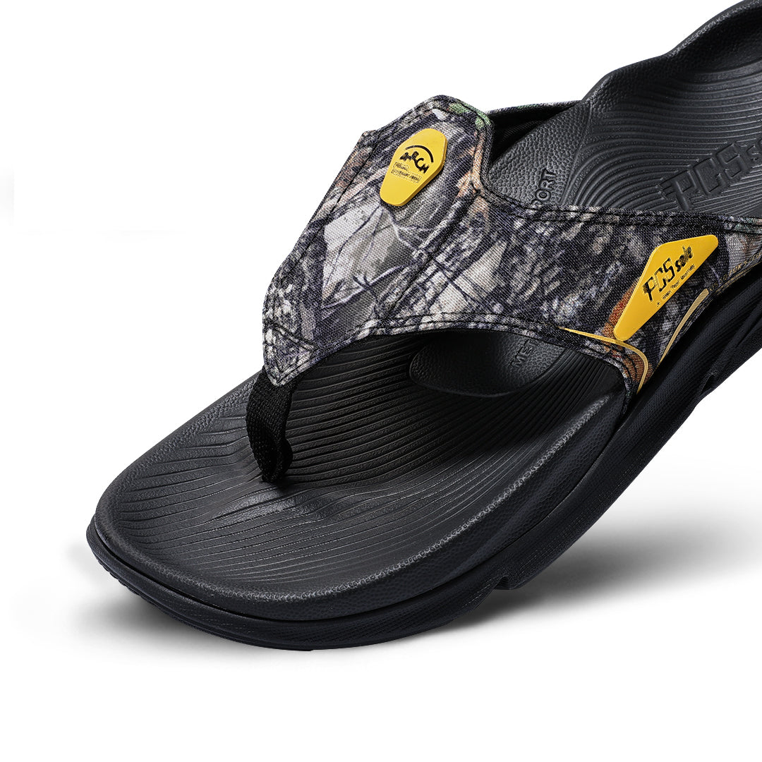A single flip-flop from PCSsole, featuring a black textured sole and footbed, a camouflage-patterned upper strap.
